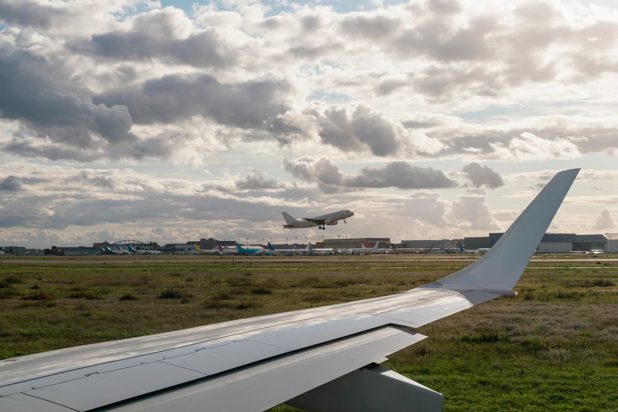 Airplane taxiing on a runway with another aircraft taking off in the background